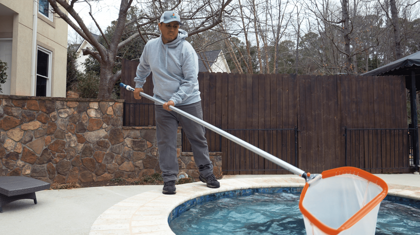 man skimming the top of an outdoor pool