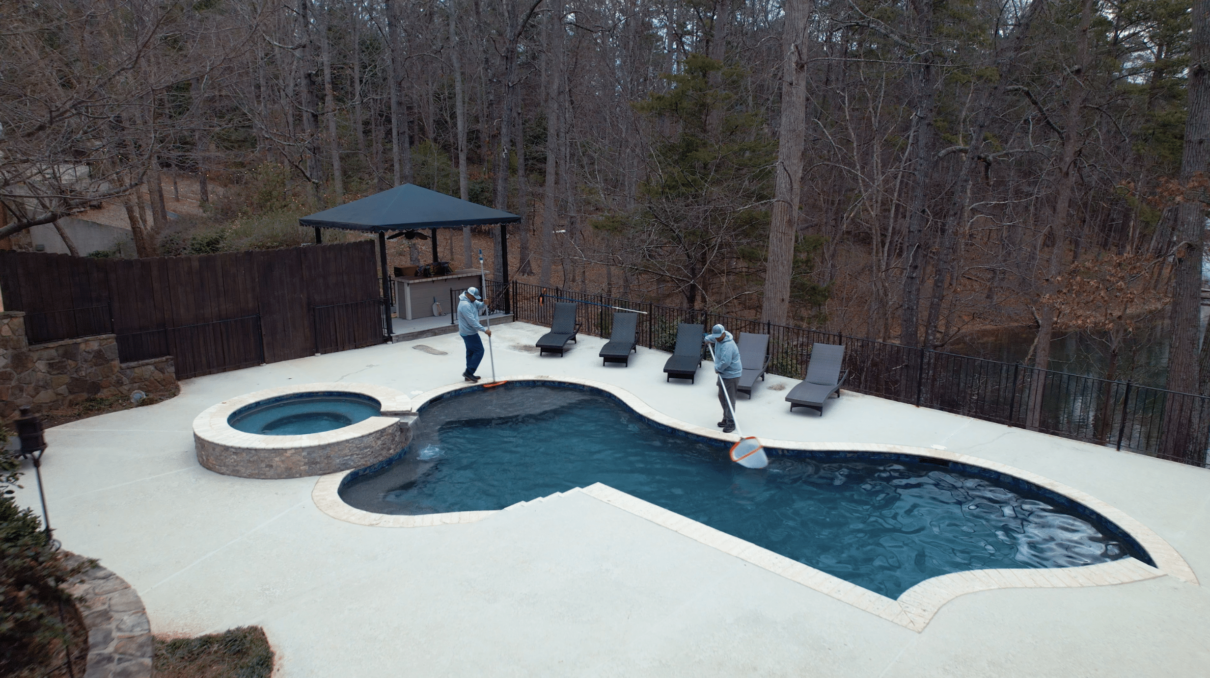 two pool cleaning technicians skimming a pool